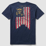 Back view of Blackbeard Glory Tee featuring a distressed American flag design with a skull and torch graphic in the upper left corner on a navy blue shirt.
