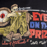 Close-up of a Black White Feather Tee featuring a detailed illustration of a soldier aiming a sniper rifle, with bold red and blue text reading "Eye on the Prize" and additional graphic elements.
