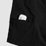 Close-up of black Field Shorts pocket with a zipper partially open, containing a white wireless earbud charging case, highlighting the pocket’s secure storage feature.