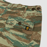 Close-up of camouflaged Fatigue Shorts pocket with button closure and small black and yellow skull logo tag on fabric.