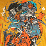 Close-up detail of a Namakubi Gold Tee featuring a vibrant graphic of a samurai warrior in traditional armor poised over a red demon against a golden yellow background.