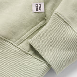 Close-up detail of the cuff and hem stitching in a soft sage green fabric on a Smuggler French Terry Crew, featuring a small woven tag with "STAY ZERO" text.