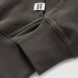 Close-up of a dark gray Smuggler French Terry Crew sleeve showing ribbed cuff detail and a small fabric tag with the text "STAY ZERO" attached near the seam.