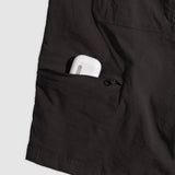 Close-up of charcoal-colored Field Shorts pocket with a zipper partially open, holding a compact white wireless earbud case.
