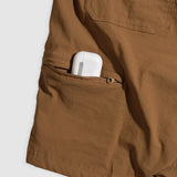 Close-up of coyote brown Field Shorts pocket with a white wireless earbud case partially visible inside the zippered compartment.