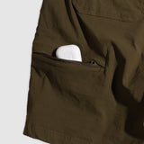 Close-up of olive green Field Shorts showing a zippered side pocket partially holding a white wireless earbud case.
