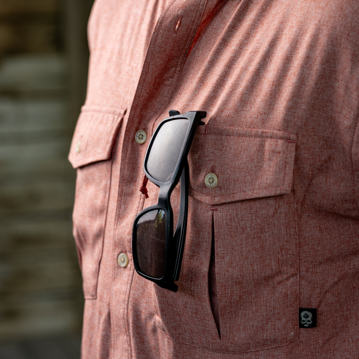 Close-up of a person wearing a reddish textured F'n Soft Daily Shirt with black sunglasses hooked onto the front pocket.