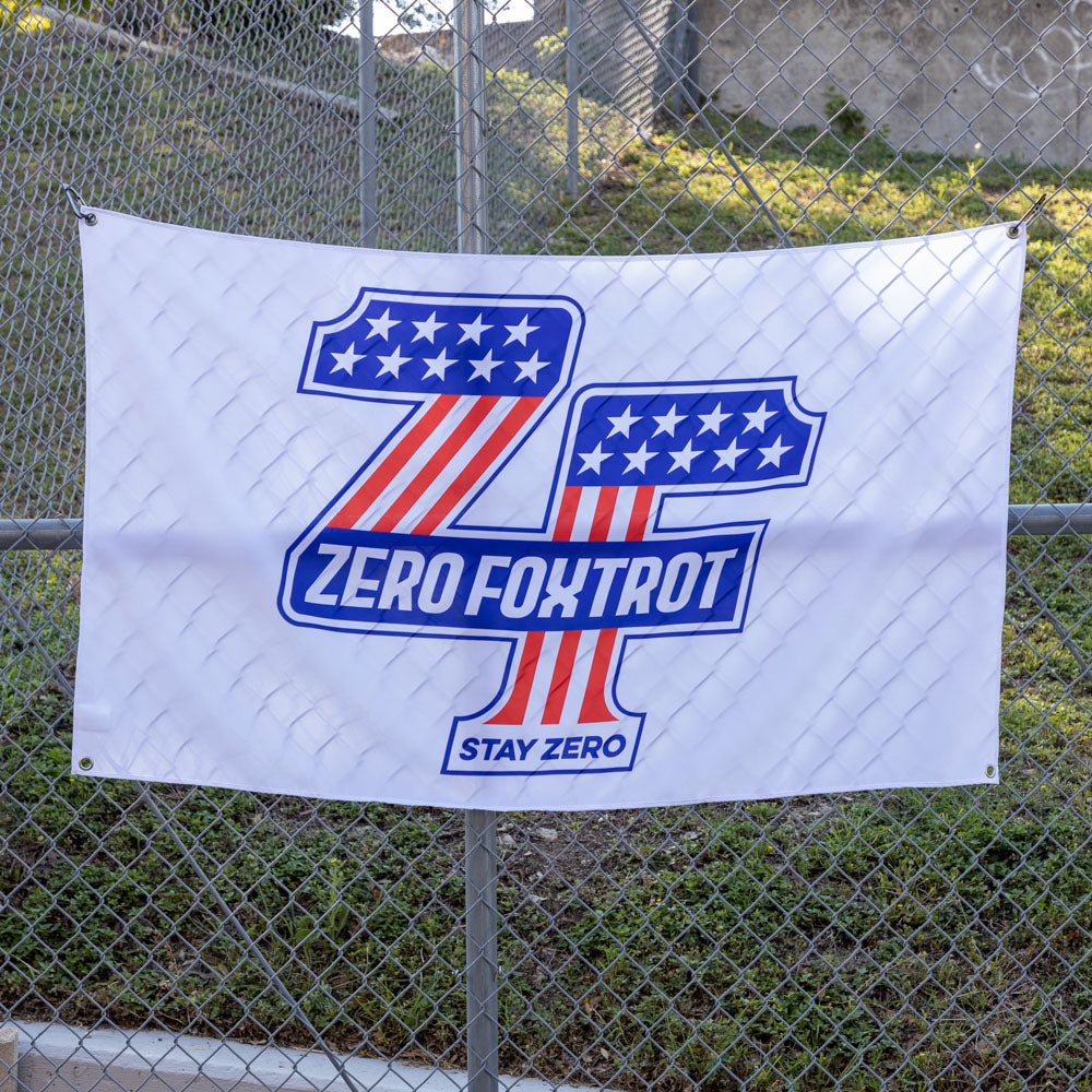 ZF Stars and Stripes Flag displayed on a chain link fence with a patriotic blue and red graphic, stars, Zero Foxtrot text, and Stay Zero slogan