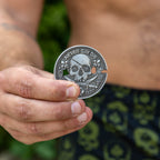 Never Say Die Coin featuring a detailed skull and crossed bones design held between fingers in a close up product photo