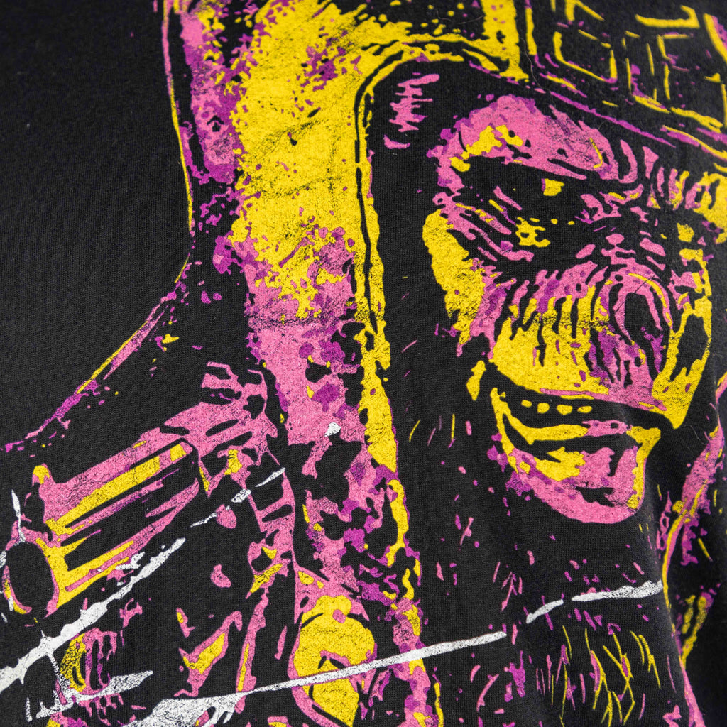 Close-up of a vibrant graphic print featuring a fierce ape face in yellow and pink tones wearing a helmet, on the black Damned Dirty Ape Tee.