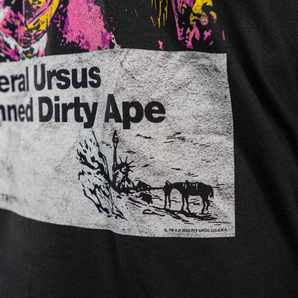 Close-up of a black Damned Dirty Ape Tee featuring a vintage-style print with text and a small graphic of horses near a rocky landscape.