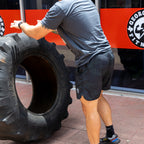 Man wearing Zero Shorts - 7" Inseam in black camo pattern flipping a large tire outdoors at a fitness gym.