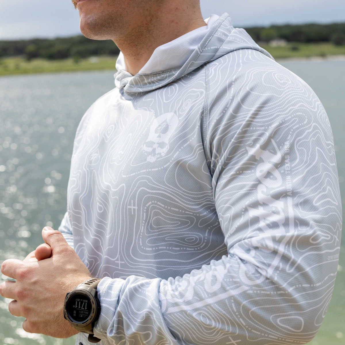 Hooded Rash Guard (Last Chance) in light gray with white contour line pattern, shown on a person outdoors near the water with a hood and long sleeves