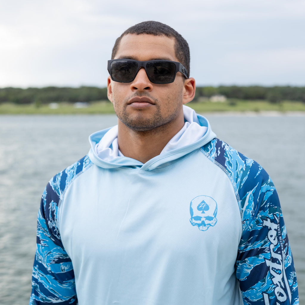 Hooded Rash Guard (Last Chance) in light blue with blue patterned sleeves, modeled outdoors by the water while wearing sunglasses