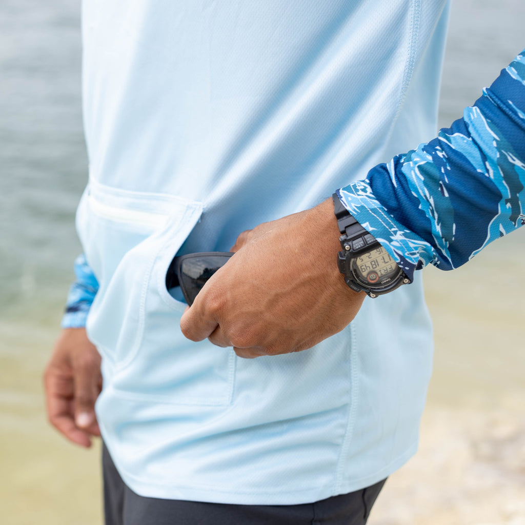 Hooded Rash Guard (Last Chance) in light blue, shown close up on a person with a hand accessing the side pocket near the waist