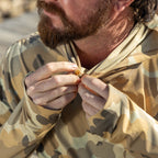 Close-up of a man fastening the hood on a camouflage-patterned Performance Sun Hoodie, highlighting the thumb holes and lightweight fabric designed for outdoor protection and comfort.
