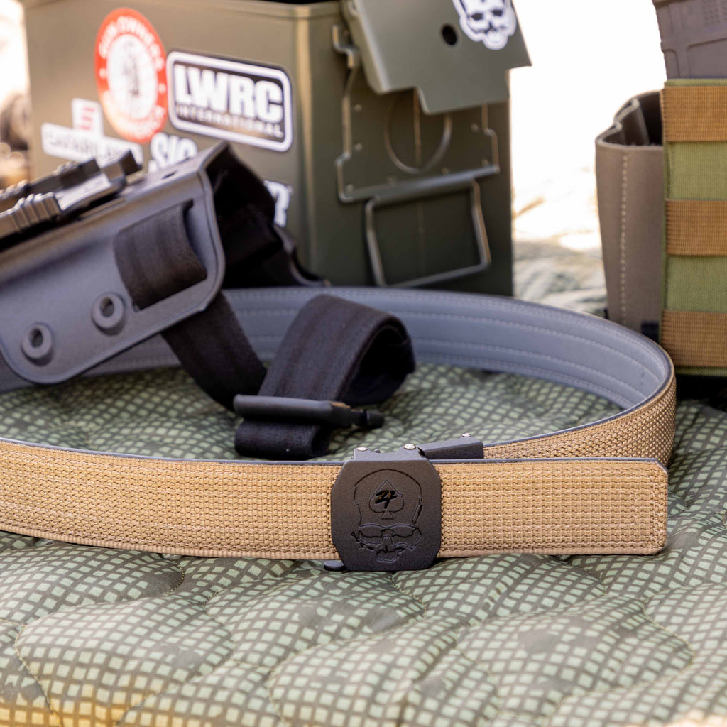 ZF x Kore Sleek Gun Belt in tan with a black buckle, shown coiled beside tactical gear and a holster on a patterned surface