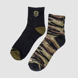 Pair of socks featuring one black sock with olive green heel, toe, and small logo, and one tiger jungle camo patterned sock in shades of green, brown, and black, labeled Zero Ankle Socks - Advisor Tiger Jungle and Black.