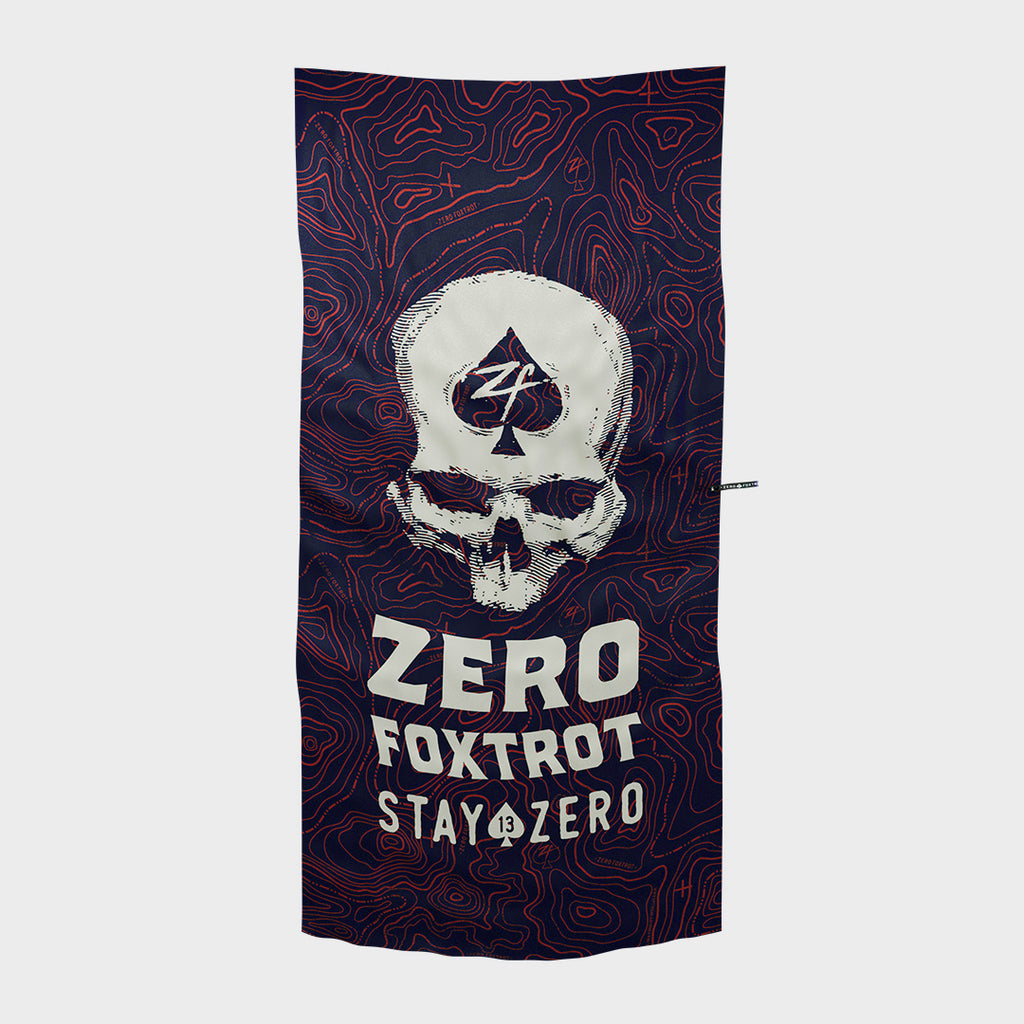 Dark microfiber beach towel featuring a white skull with a spade symbol and the text "Zero Foxtrot Stay Zero" over a red topographic map design, part of the Microfiber Beach Towels collection.