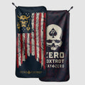 Microfiber Gym Towel featuring a dark background with a distressed American flag design including a skull and flame graphic, paired with a matching carrying pouch displaying a skull and spade emblem.