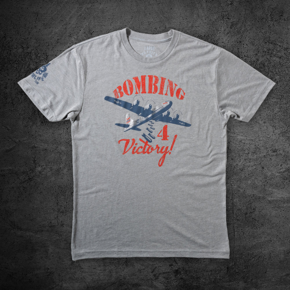 Bombing For Victory Tee gray T shirt featuring a blue airplane graphic and red Bombing For Victory lettering displayed flat on a dark background