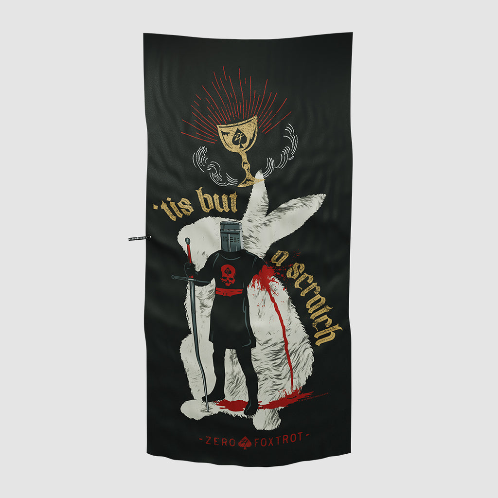 Black microfiber beach towel featuring a medieval knight standing in front of a large white rabbit with a golden chalice above and the phrase "'tis but a scratch" in decorative gold lettering.