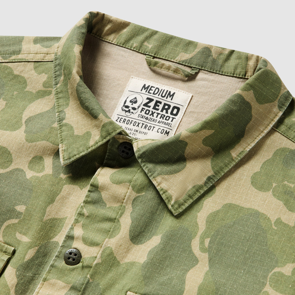 Close-up of a medium-sized CPO Shirt featuring a green and tan camouflage pattern with a classic collar and black buttons.