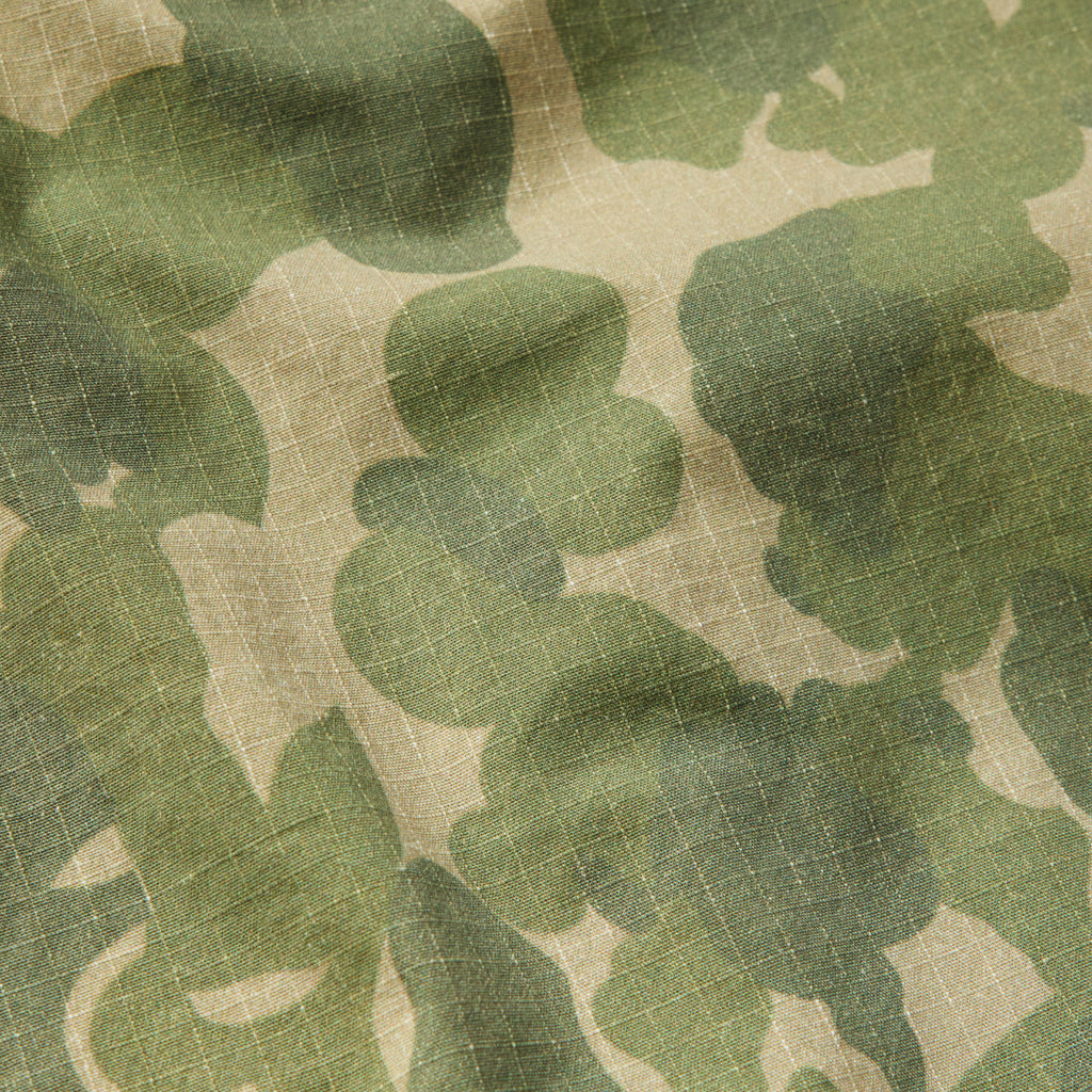 Close-up of green and beige camouflage fabric with a subtle grid pattern, showcasing the texture and material of the CPO Shirt.