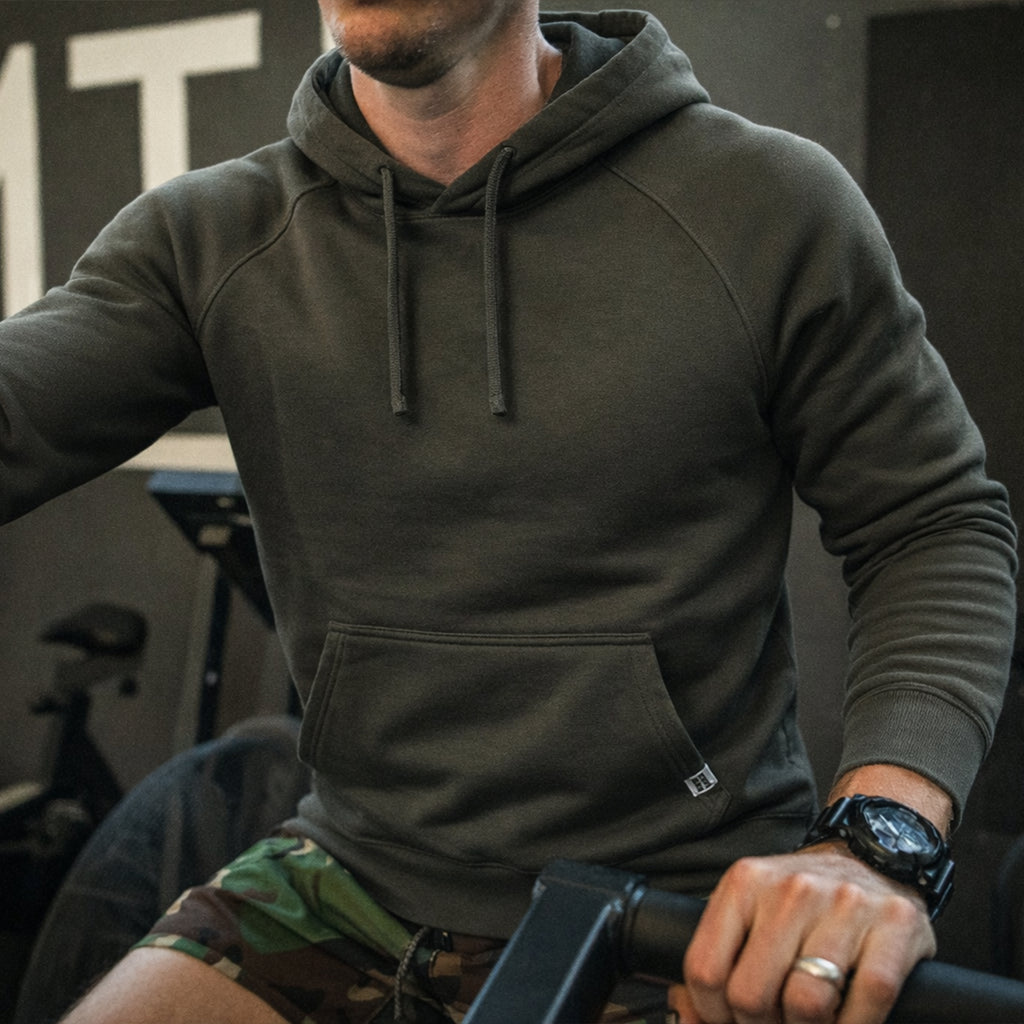 Man wearing a dark charcoal Smuggler French Terry Hoodie with front pocket and adjustable drawstring hood while exercising indoors.