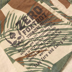 Close-up of a fabric label on a Chore Jacket featuring a camouflage pattern and printed text with military-inspired design elements.