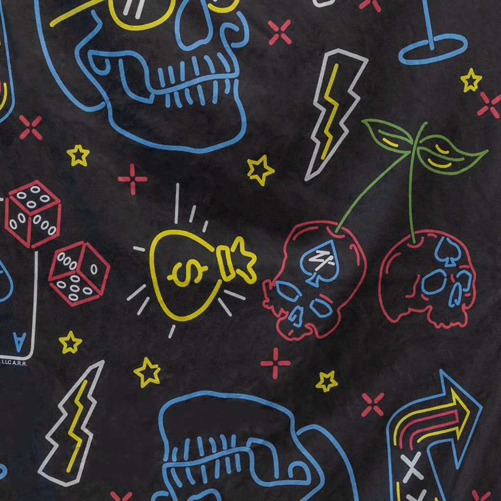 Close-up of a black microfiber fabric with colorful neon-style illustrations including skulls, cherries, dice, lightning bolts, stars, and a money bag, part of the Microfiber Beach Towel (2025).