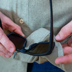 Close-up of a person holding black sunglasses and wearing a light beige buttoned shirt made of soft fabric, showcasing the texture and detail of the F'n Soft Daily Shirt.