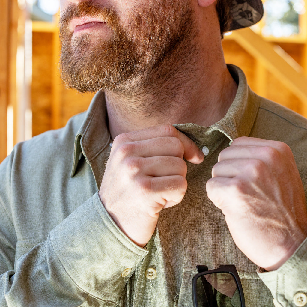 Close-up of a man adjusting the collar of his olive green F'n Soft Daily Shirt, highlighting the soft fabric texture and casual fit in natural daylight.