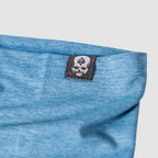 Close-up of a light blue fabric edge with a black tag featuring a white skull and spade logo, part of the Performance Sun Gaiter accessory.