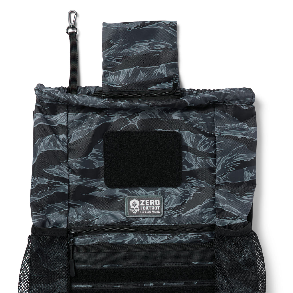 TAC Drawstring Pack in black and gray tiger stripe pattern with multiple compartments, mesh side pockets, and a top flap with a clip attachment.