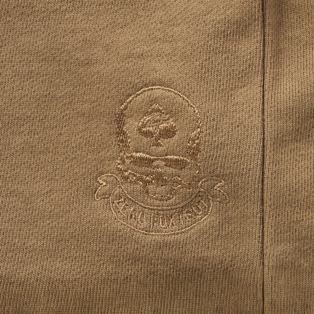 Close-up of embroidered skull and spade emblem on brown fabric of Smuggler French Terry Zip Hoodie, highlighting detailed stitching and textured material.