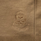 Close-up of embroidered skull and spade emblem on brown fabric of Smuggler French Terry Zip Hoodie, highlighting detailed stitching and textured material.
