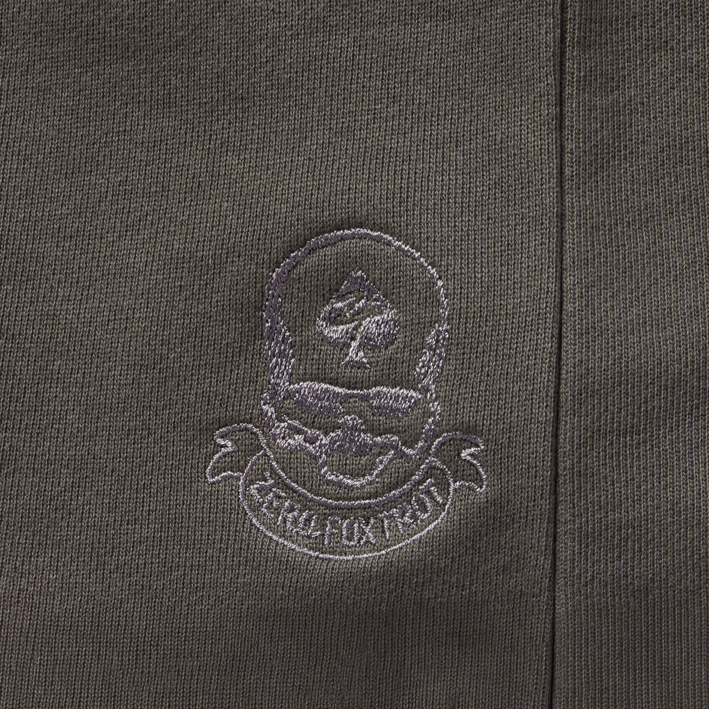 Close-up of a dark fabric with a stitched skull and spade emblem and a banner detail, featured on the Smuggler French Terry Zip Hoodie.