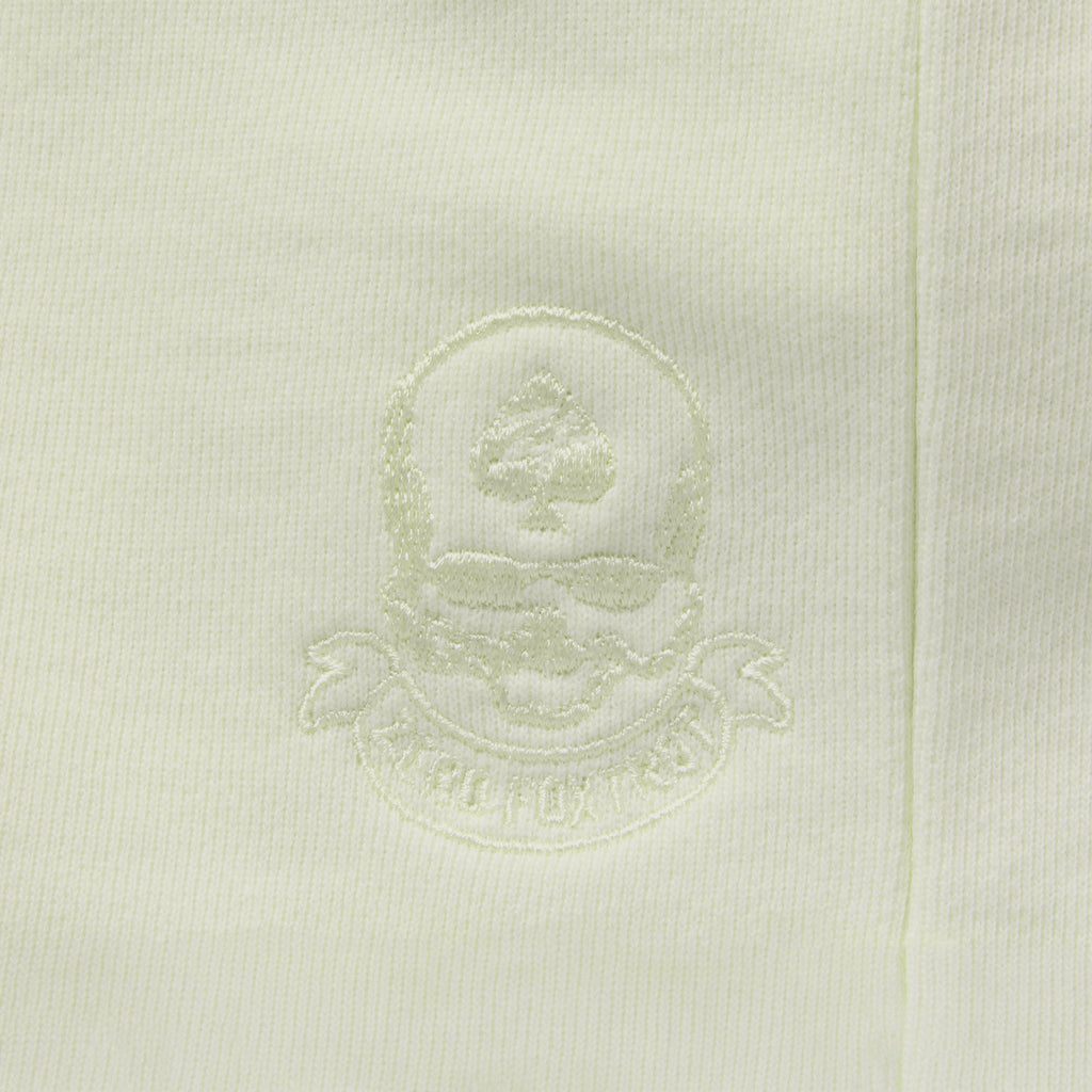Close-up of a light sage green Smuggler French Terry Hoodie featuring a subtle embroidered skull and ace of spades logo on soft French terry fabric.