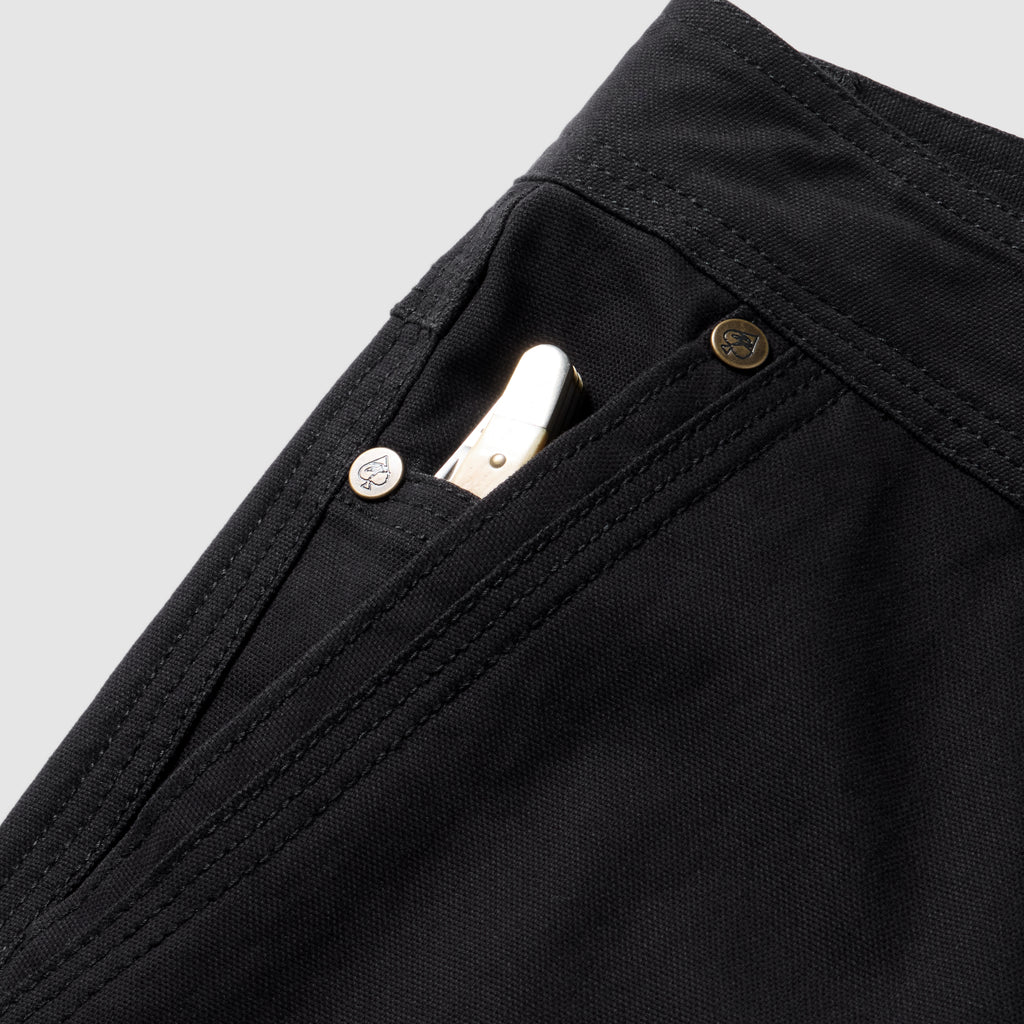 Foxhole 5 Pocket Pant in black with a close up view of the front pocket stitching and metal rivet detail and a white item tucked inside