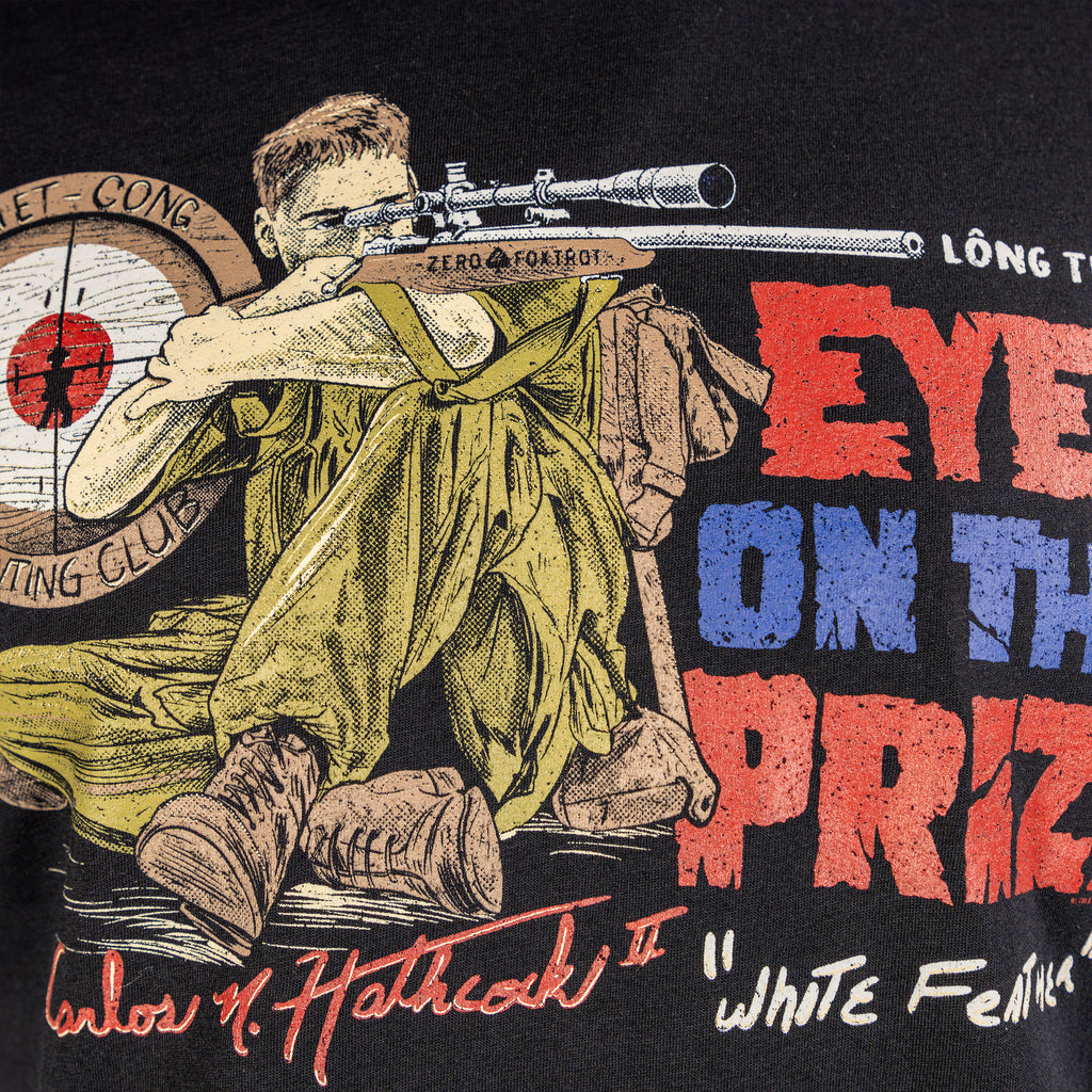 Close-up of a Black White Feather Tee featuring a detailed illustration of a soldier aiming a sniper rifle, with bold red and blue text reading "Eye on the Prize" and additional graphic elements.