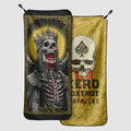 Two microfiber gym towels displayed, one featuring a detailed design of a crowned skeleton with red accents, the other showing a skull with a spade symbol and text on a yellow background.