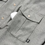Close-up of a charcoal gray textured fabric pocket with button closure and a small black skull tag detail on the F'n Soft Daily Shirt, showing part of the button-up front.
