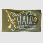 Hate Keeps Me Warm Flag in olive green with blue and cream lettering, featuring a rifle graphic, skull emblem, and distressed military inspired artwork