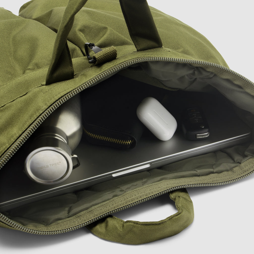 ZF Flyers Helmet Bag open in olive green, showing a laptop, stainless steel bottle, wireless earbuds case, and smartphone inside the zippered compartment