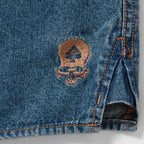 Denim Work Shirt close up showing blue denim fabric, reinforced stitching, side seam, and a small embroidered emblem near the hem