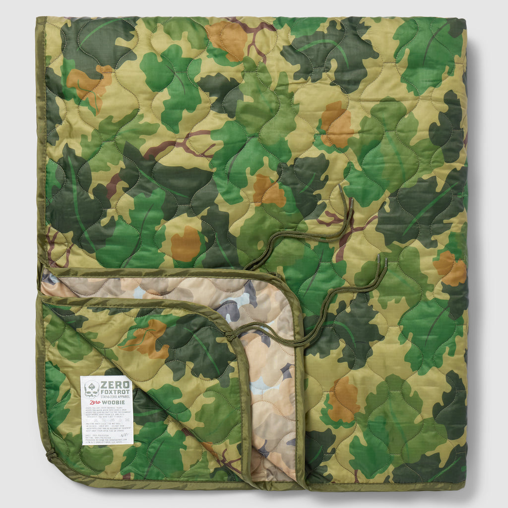 Woobie Blanket folded in a green woodland camouflage pattern with quilted fabric and a visible sewn label on the front panel