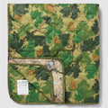 Woobie Blanket folded in a green woodland camouflage pattern with quilted fabric and a visible sewn label on the front panel