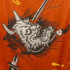 Close-up of an orange microfiber beach towel (2025) featuring a detailed graphic of a stylized horned demon head pierced by a sword.