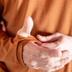 Close-up of a person's hands adjusting the thumb hole on the cuff of a rust-colored Performance Sun Hoodie sleeve, highlighting the fabric texture and fit.